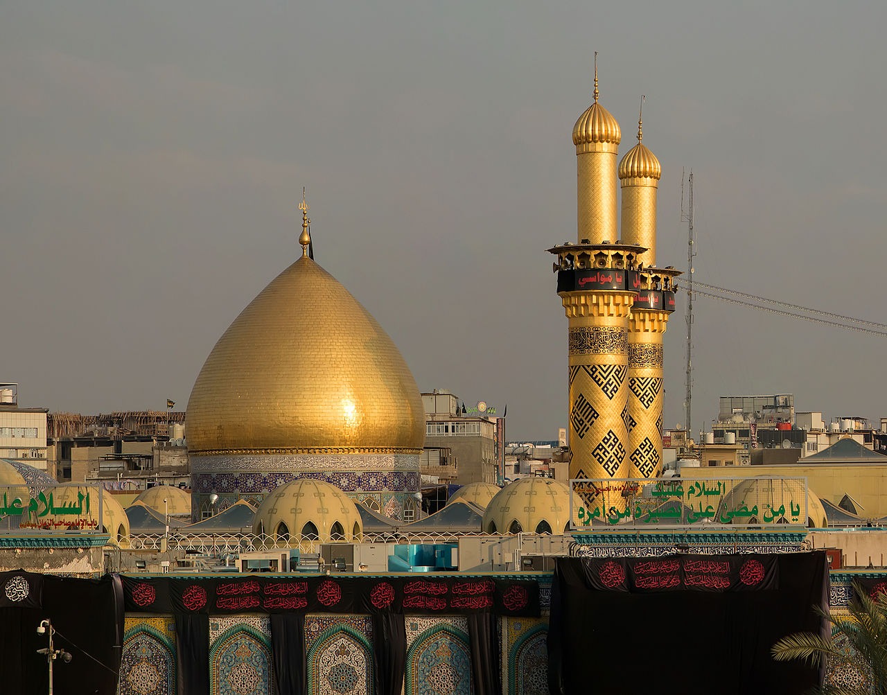 Golden dome and twin golden minarets of the al-Abbas shrine in Karbala, with black mourning banners on the outer wall