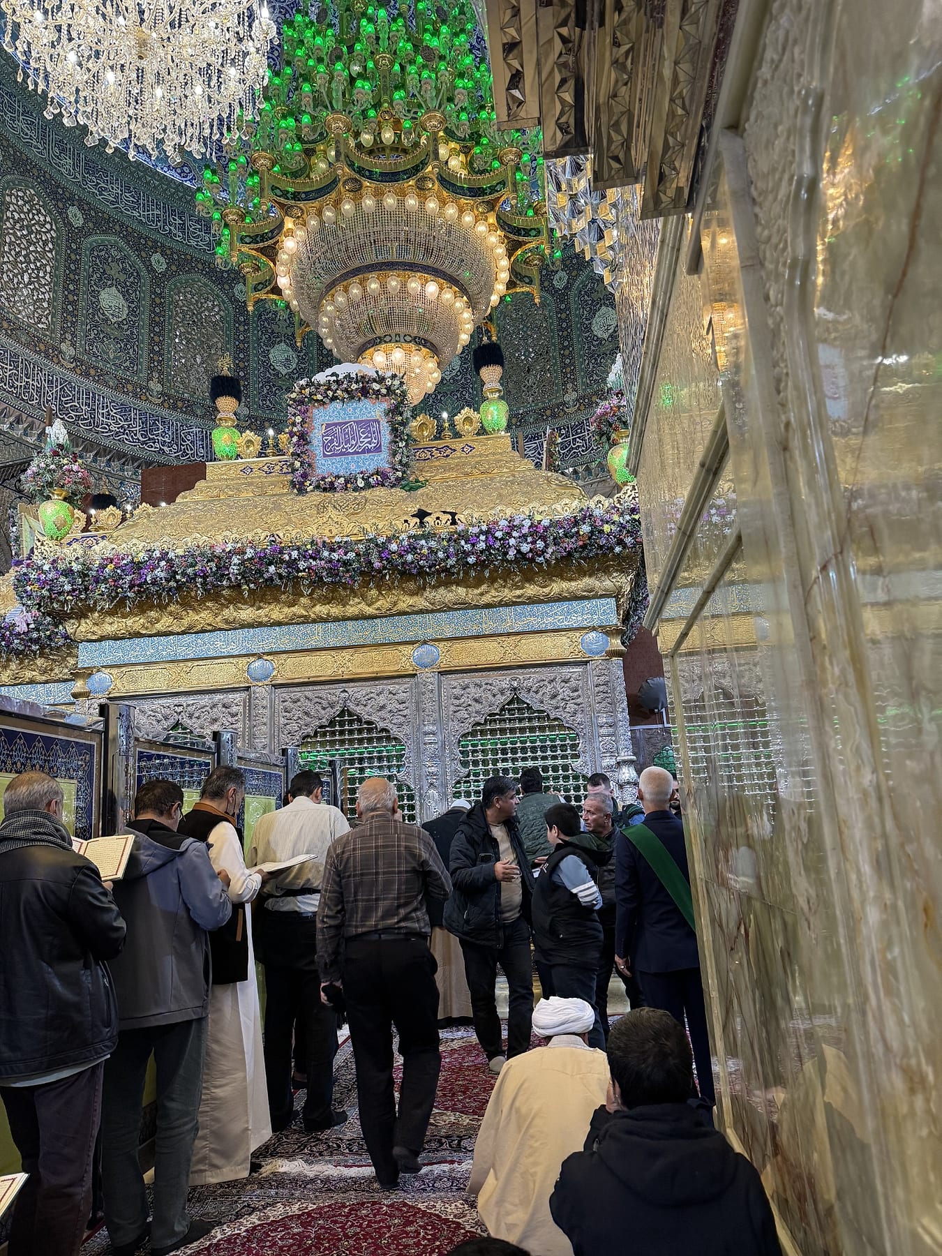 Visitors gathered in front of an ornate gilded enclosure beneath a large chandelier