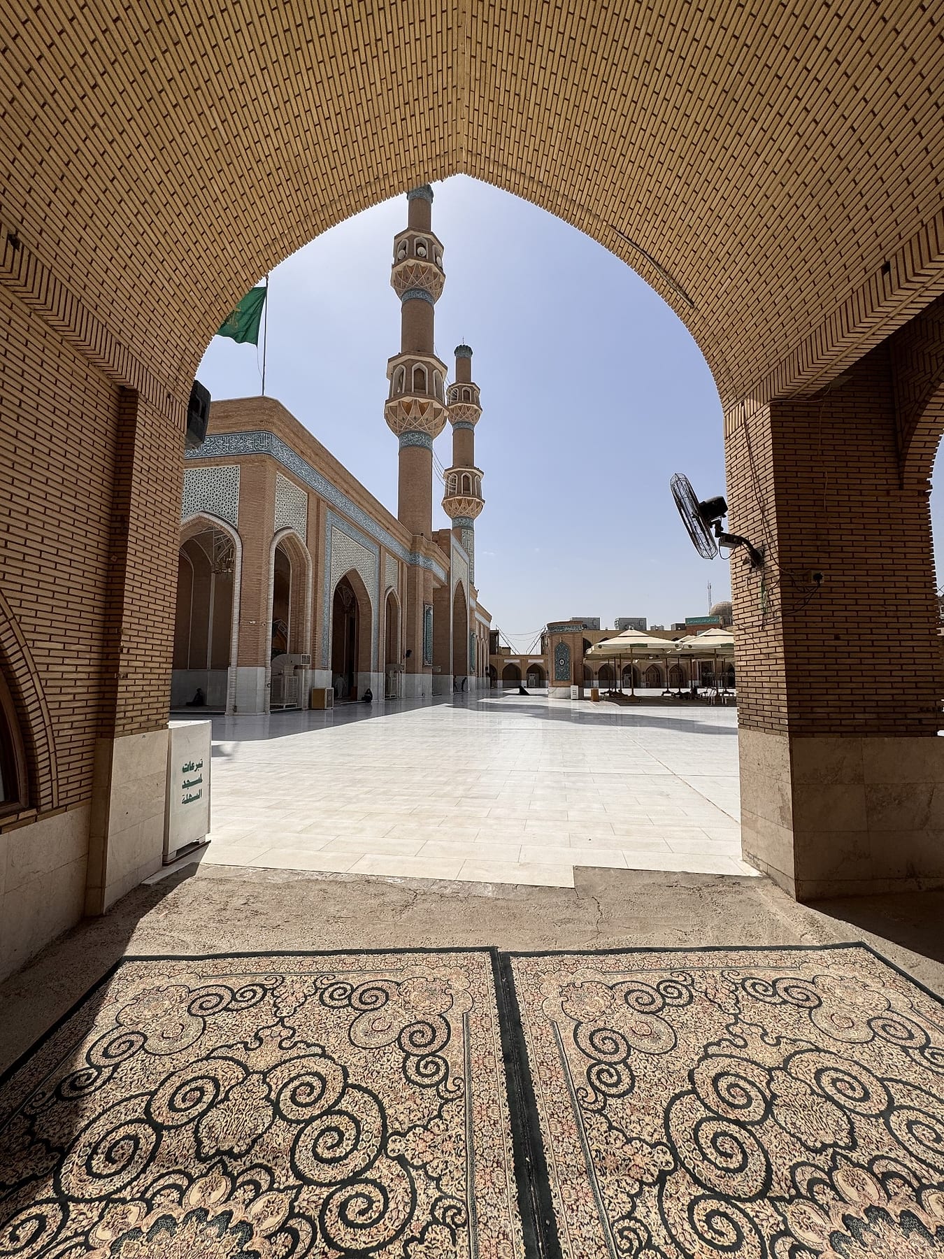 The open courtyard and minarets framed by a deep brick archway, with patterned carpet in the foreground