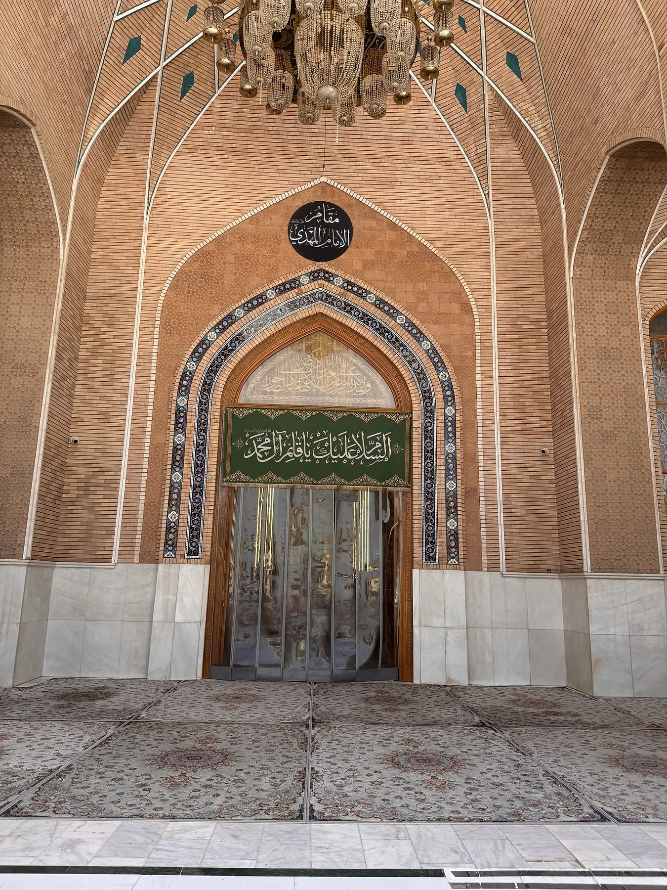 A tiled pointed portal set into a high brick wall, with a green banner above the doors