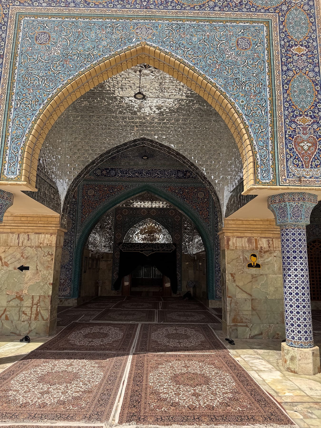 A tiled arched porch leading into the shrine, with carpets laid on the floor